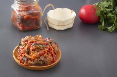 Cam kavanozun, domatesin ve yeşilliğin arka planına karşı gri bir masada, ahşap bir tabakta sebzeli haşlanmış patlıcan. Ev yapımı. Boşluğu kopyala