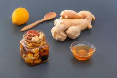 Ceviz, kaju, kuru üzüm, kurutulmuş kayısı ve kuru erik karışımı cam bir kavanozda bal, bir kaşık, zencefil ve limon ile gri bir masada.