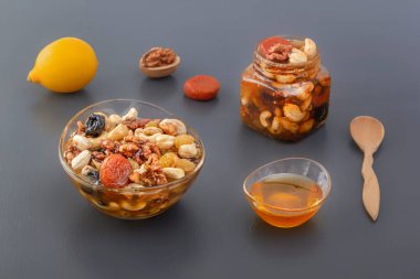 İçi ceviz, kaju, kuru üzüm, kuru kayısı, bal, malzeme ve limon karışımıyla dolu cam bardak ve kavanoz.