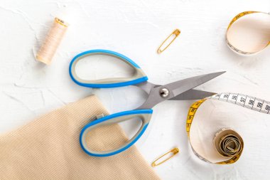Açılmış makas, terzinin mezurası, beyaz arka planda iplikler ve iğneler. Üst görünüm