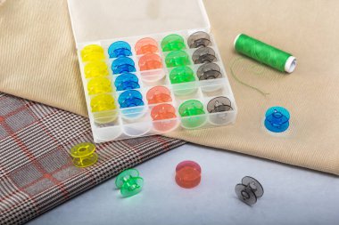 Kutudaki iplikler için çok renkli bobinler kumaş parçalarının üzerinde yatıyor.