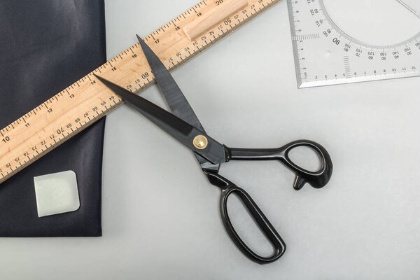 Open tailor's scissors, patterns, markers and cuts of material lie on the table. View from above