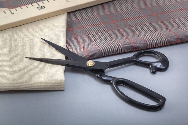 Open tailor's scissors lie with a wooden meter on cuts of material. Close-up