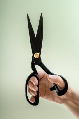 Tarafsız bir arkaplanda kadın elinde terzi makası açık. Yakın plan.
