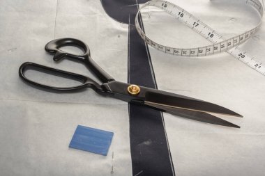 Terzinin makası dikiş aksesuarlarının arka planına karşı boş bir kumaş ve kağıt deseninin üzerinde yatar. Yakın plan..