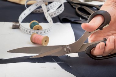Bir kadının elindeki terzi makası kağıt kalıplarına göre kumaşı kesmiş. Yakın plan.