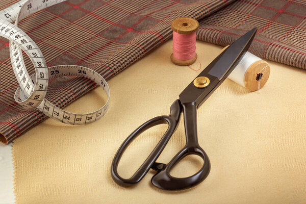 Tailor's scissors lie on a fabric blank against the background of sewing accessories. Close-up.