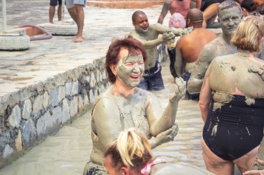 Dalyan, Turkey - May 9, 2022. Laughing woman smears herself with therapeutic mud in the pool against the background of other people. Close-up
