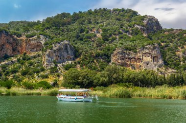 Dalyan, Turkey - May 9, 2022. Tourist pleasure boat on the river next to the rocks in which the Lycian tombs are located