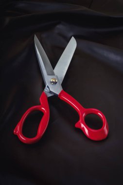 Open scissors with red handles lie on a piece of dark material. Close-up
