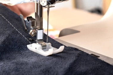 Sewing machine foot with a needle sews fabric. Close-up. Place for text