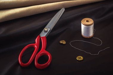 Terzinin makası dikiş aksesuarlarının arka planına karşı boş bir kumaşın üzerinde yatar. Yakın plan..