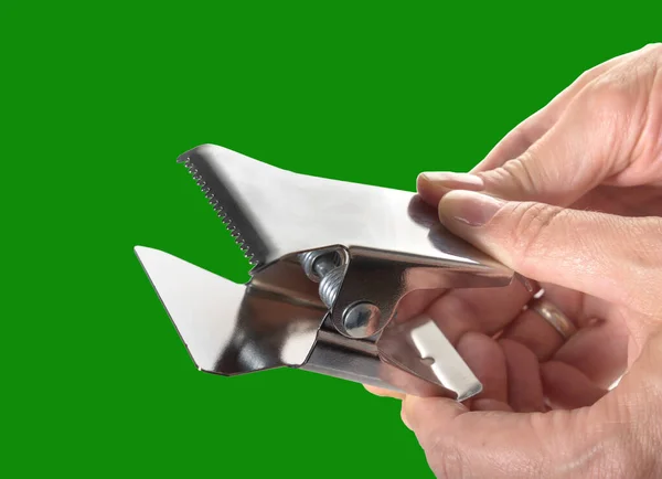 Woman\'s hand holds a metal clip for cutting fabric on a neutral green background. Isolated