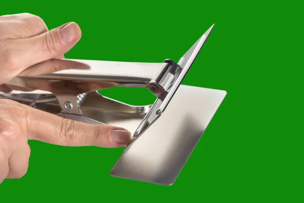 Woman's hand holds a metal clip for cutting fabric on a neutral green background. Isolated