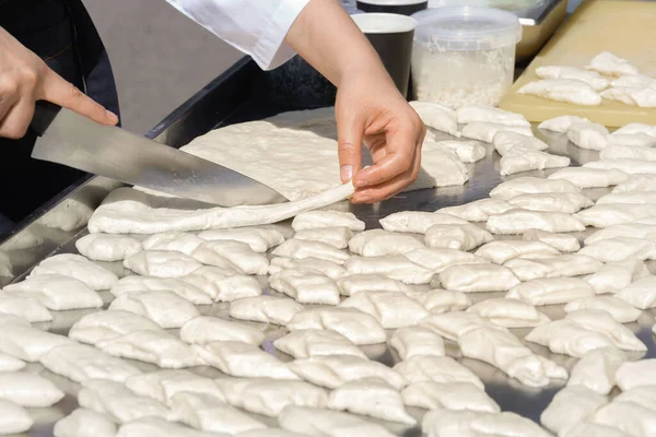 Hands of the cook with a large kitchen knife cut dough pieces for frying on a street food tray