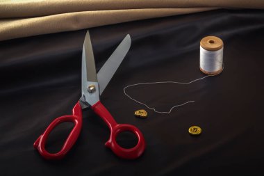 Terzinin makası dikiş aksesuarlarının arka planına karşı boş bir kumaşın üzerinde yatar. Yakın plan..