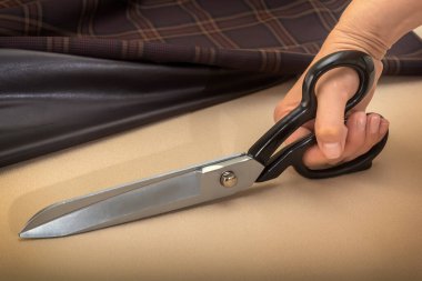 Tailor's scissors in a woman's hand are preparing to cut the fabric. Close-up