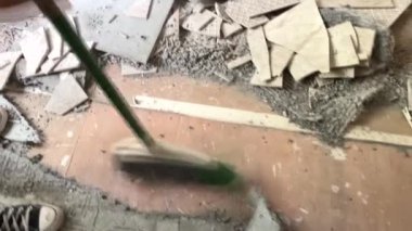An unrecognizable man cleans up broken tiles in a home remodeling project.