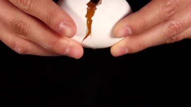 Kadınların elleri beyaz yumurtaları kırıyor. Yumurtanın sarısı dökülüyor. Siyah arka planda yemek pişiren tanınmamış kadınlar. Kapatın. Yüksek kaliteli FullHD görüntüler