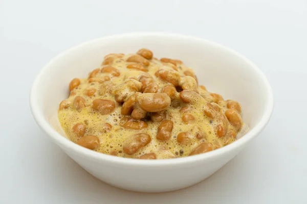 Beyaz arka planda bir kasede nefis görünen natto.