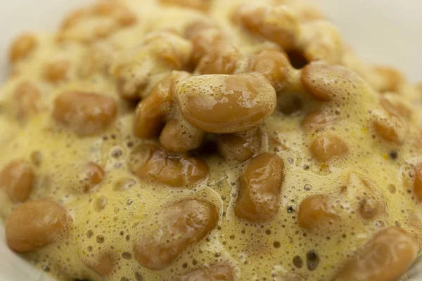 Beyaz arka planda bir kasede nefis görünen natto.