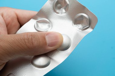 Mavi arka planda tek tek paketlenmiş haplar.