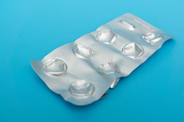 Mavi arka planda tek tek paketlenmiş haplar.