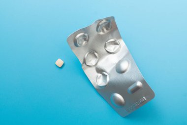 Mavi arka planda tek tek paketlenmiş haplar.