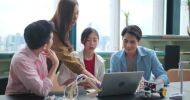 Bir grup Asyalı lise öğrencisi bir teknoloji robotu için yenilenebilir enerji projesi programlamak için dizüstü bilgisayar kullanıyor. İş arkadaşları rüzgar enerjisini tartışıyor ve bunu test ediyorlar..