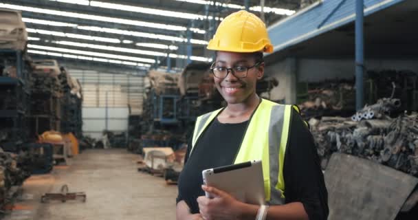 在工厂里 穿着安全帽的非洲裔美国黑人女工拿着平板相机看着汽车发动机零件 面带微笑 产业工人概念 — 图库视频影像
