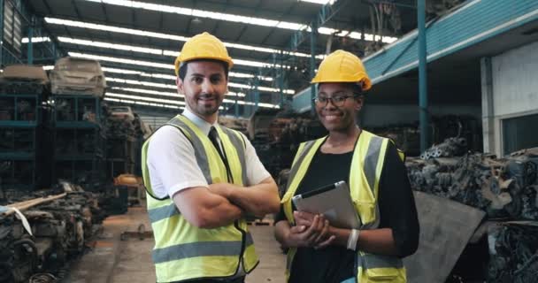在老汽车配件制造厂 两名多文化微笑的工人 非洲黑人女性和美国男性技师 戴着安全帽 看起来像相机 产业工人概念 — 图库视频影像