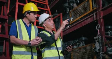 Güvenlik kaskı takan, endüstriyel beyaz ve Asyalı işçilerin iki portresi araba endüstrisindeki kullanılmış otomobil parçalarını kontrol ediyor..