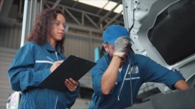 İki oto tamircisi araba motorunu kontrol ediyor ve araba tamirhanesinde notlar alıyor. Araba tamiri ve bakımı. Otomotiv servisinde çalışan araba tamircisi..