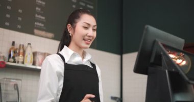 Asyalı kadın barista çalışanı müşteriyle video görüşmesi sipariş ürünlerini çevrimiçi olarak satarak tablet dokunmatik ekranda tablet kahve dükkanında veya restoranda sosyal medya satın alıyor..
