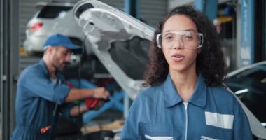 Üniformalı araba tamircisinin portresi kameraya garajdaki araba tamirini ve araba servisi konseptini açıklıyor.