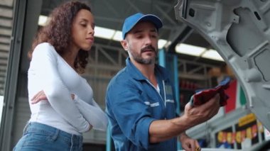 Tamirci kadın müşteriye motor yağı seviyesini kontrol ediyor ve tamirhanede aracının tamirini tartışıyor..