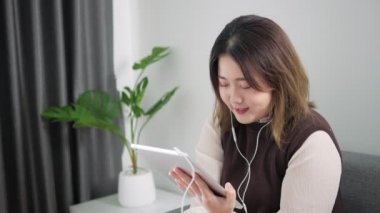 Tablet kullanan Asyalı kadın evdeki oturma odasında müşteriyle video konferansı yapıyor, evden çalışıyor..