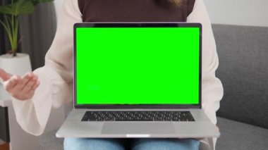 Evdeki kanepede yeşil ekran ve krom anahtar modeli olan kadın sunumu laptopu. Yeşil ekran gösteriliyor ve kamerayla konuşuyor