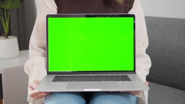 女人在家里的沙发上展示带有绿色屏幕和彩色键的笔记本电脑 显示绿色笔记本电脑屏幕完美的产品放置 — 图库视频影像