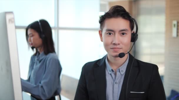 形象的亚洲商人微笑着对着相机头戴耳机在办公室里推销客户服务代理团队 为遥远的客户提供支持 呼叫中心工作概念 — 图库视频影像