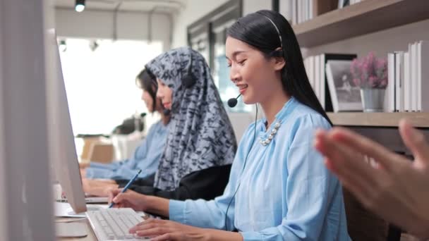 コールセンターオフィスでチームサポートを持つカスタマーケアオペレーターとして働くマイクヘッドセットを身に着けているアジアのビジネス女性 — ストック動画