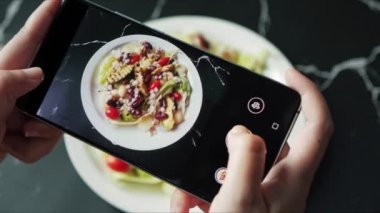 Sosyal medyada paylaşmak için güzel yeşil salata avokadosunun fotoğrafını çeken akıllı telefon kullanan yemek blogcusu.