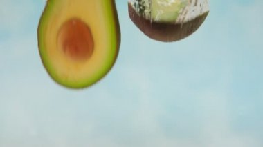 Mavi arka planda suya düşen taze avokadonun Yavaş Hareketi, sağlık için sebzeler.