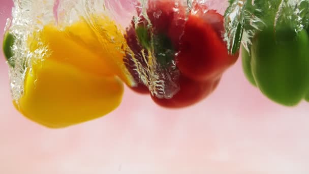 Tři Papriky Červené Žluté Zelené Padající Vody Stříkance Růžovém Pozadí — Stock video