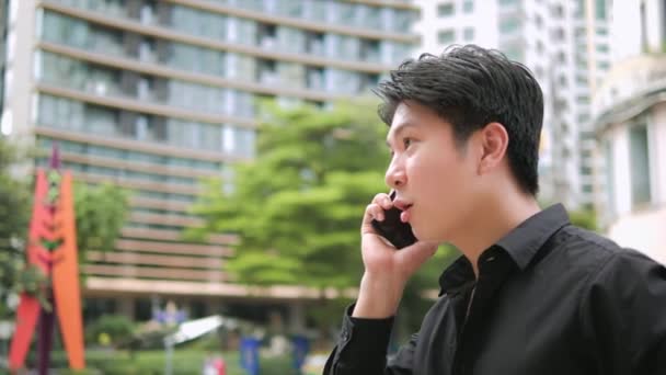 都会の通りで屋外でスマートフォンで話す若いアジア人ビジネスマンを自信を持って — ストック動画