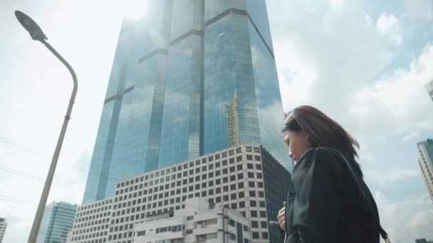 アジアの従業員ビジネス女性のバックビュースーツの建物を介して太陽光と現代都市のビジネス街の中心部を歩く — ストック動画
