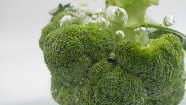 白い背景に水のスプラッシュに陥る緑のブロッコリーのスローモーション 健康のための野菜 — ストック動画