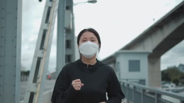 都市部の空の通りで一人でランニングやジョギングをしている若いアジアの女性にフィット保護のための保護顔マスクを身に着けていますほこりや汚染や保護ウイルス — ストック動画