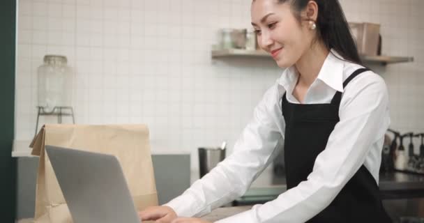 アジアの女性のウエイトレスのレジ係は ラップトップ上の顧客からオンライン注文コーヒーやパン屋を入力します 小規模事業主とパートタイムの仕事のコンセプト — ストック動画