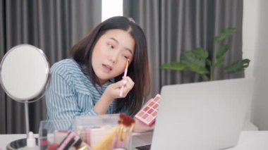 Genç Asyalı kadın güzellik blogcusu ve çevrimiçi makyaj kursu laptop.Makyaj dersini evde canlı yayında kullanıyor.